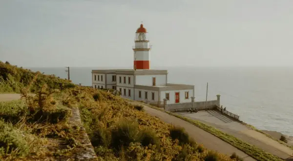 El faro de Baiona se alza majestuoso sobre un acantilado cubierto de vegetación dorada, vigilando el mar.