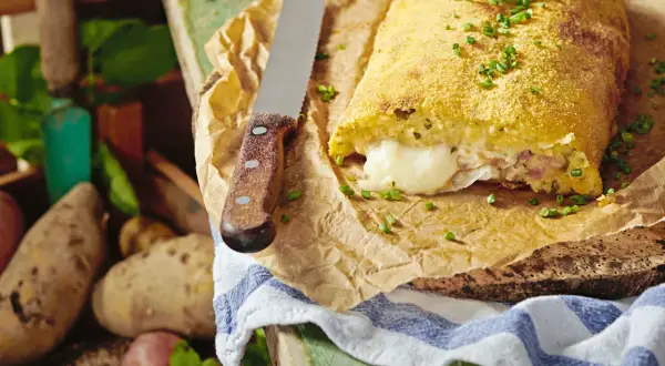 Herzhaft gefüllte polpette di patate, goldbraun paniert, mit geschmolzenem Käse im Inneren. Frische Kartoffeln liegen daneben.