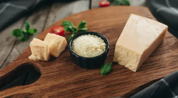 Kawałek parmezanu, pokrojony ser i starty ser do carbonary na drewnianej desce, ozdobione bazylią i pomidorkami.