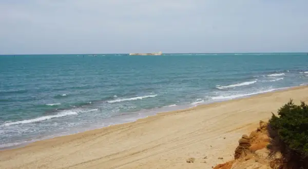 Playa de arena dorada con mar turquesa y una estructura en el horizonte. Un rincón idílico de las calas Chiclana.