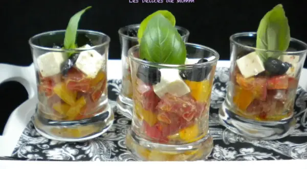 Quatre verrines apéro colorées avec tomates, olives, feta et basilic, présentées sur un plateau décoré.