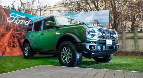 Zielony Ford Bronco prezentuje się imponująco na tle krajobrazu z pustynią i logo Ford.