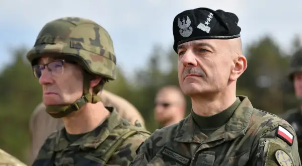 Generał Andrzejczak w czapce z orłem i gwiazdkami, obok żołnierz w hełmie.