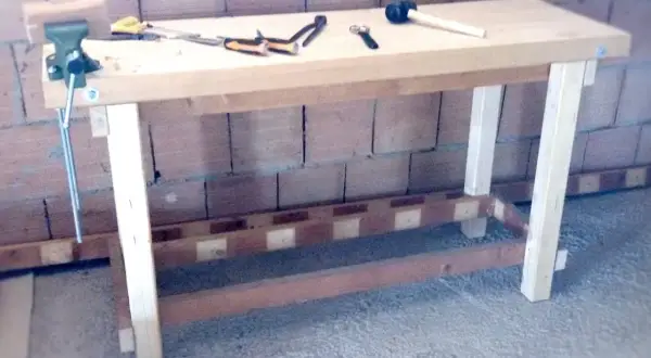 Un banco da lavoro in legno, pronto per iniziare a fare un tavolo in legno. Attrezzi come morsa, martello e pinze sono pronti all'uso.
