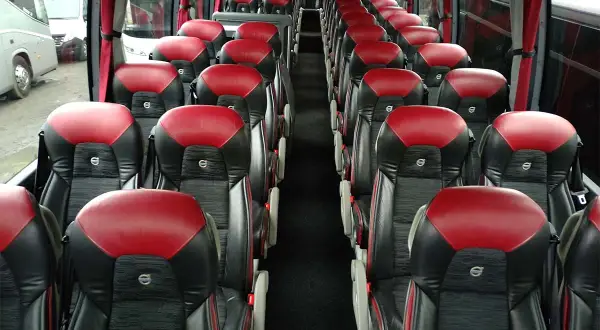 Wnętrze autobusu z rzędami czerwono-czarnych siedzeń. Zastanawiasz się, ile może jechać kierowca, gdy wszyscy pasażerowie są już na swoich miejscach.