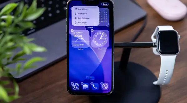 Nowy iPhone z najnowszym iOS, pokazujący widżety pogody i zegara. Obok stoi Apple Watch.