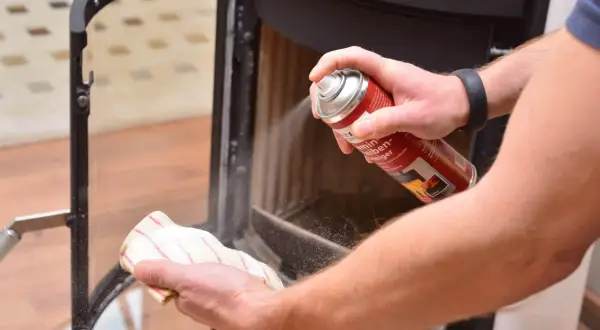 Hände reinigen den Kamin: Mit einem Reiniger wird der Ruß vom Schamottstein und Glas entfernt.