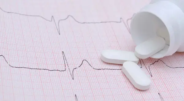 Vita tabletter, potentiellt betablockerare ångest, ligger utspridda på ett EKG-papper.