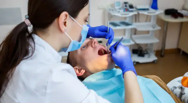 Dentystka bada zęby pacjenta. Czy dentysta może wystawić L4? Tak, jeśli stan zdrowia pacjenta tego wymaga.