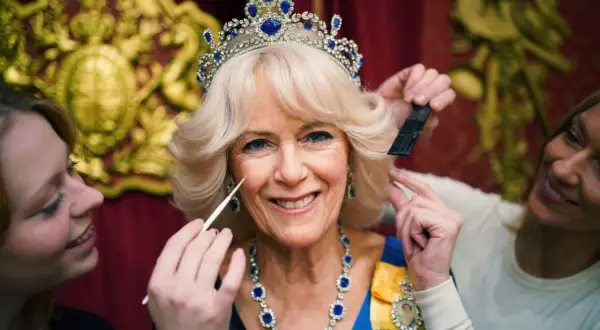 Camilla, drottningen, får smink och hår fixat. Hon bär en tiara och ett blått halsband.