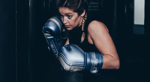 Focused boxer in blue gloves, ready to spar. She looks determined, like a light heavyweight facing a cruiserweight challenge.