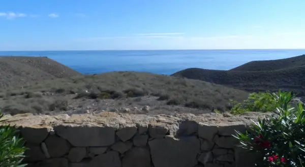 Vista desde una mesa roldan, con el mar azul al fondo y colinas áridas cubiertas de vegetación baja.
