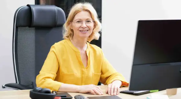 Uśmiechnięta wicedyrektor w żółtej bluzce siedzi przy biurku, gotowa do pracy.