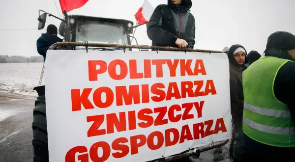 Rolnicy protestują z transparentem "Polityka komisarza zniszczy gospodarza" na tle traktora.