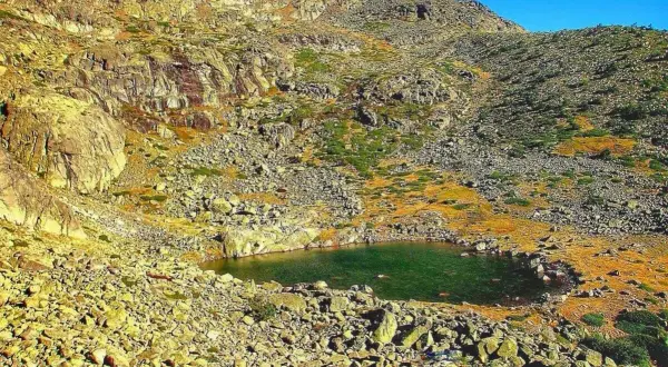 Laguna en la ruta de Peñalara, rodeada de rocas y vegetación de montaña bajo un cielo azul.