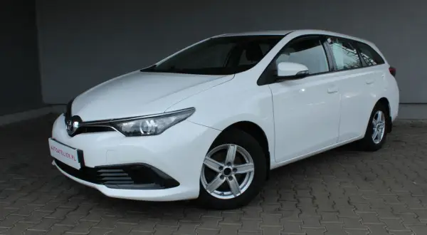 Biała Toyota Auris II 1.6 132 KM, kombi, na chodniku. Wiele osób szuka o niej pozytywnych opinii.