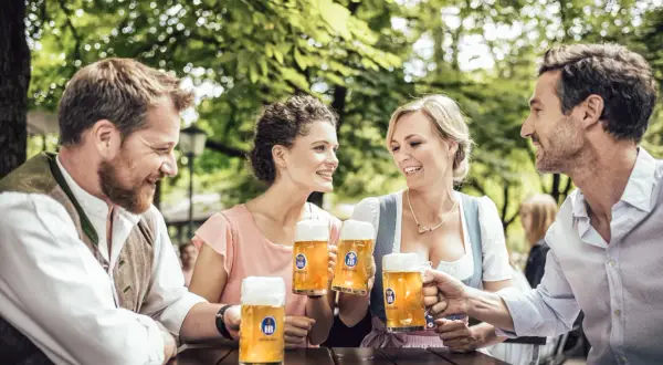 Coppie brindano con boccali di zwickl birra sotto alberi verdi.