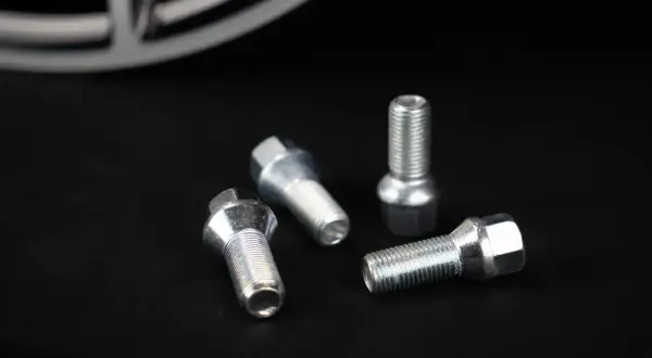 Cztery śruby do felg aluminiowych leżą na czarnym tle. Zastanawiasz się, jakie śruby do felg aluminiowych wybrać?