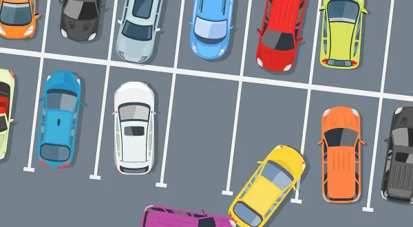 Bunte Autos auf einem Parkplatz. Ein gelbes Auto biegt von der Parkplatz Ausfahrt ab, Vorfahrt beachten.