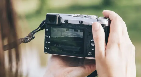 Dłonie trzymają aparat, który może być dobrym aparatem fotograficznym do 500 zł. Na ekranie widać krajobraz.