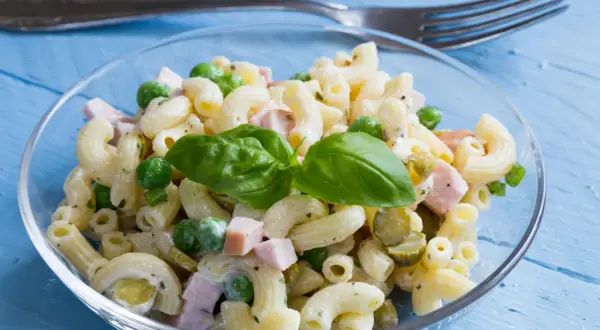 Ein cremiger Nudelsalat mit Erbsen, Schinken und Gurken, garniert mit Basilikum. Perfekt als schnelles rezept nudelsalat.