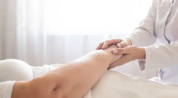 Delikatne dotknięcie dłoni pielęgniarki na ramieniu pacjenta, wskazujące na troskę i pomoc w procesie, jak wyleczyć odleżyny.