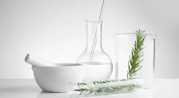 Laboratorio con mortaio, provette e becher contenenti rosmarino e liquido limpido, forse benzyl alcohol per estrarre essenze naturali.