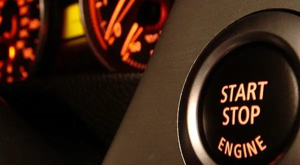 Bouton "START STOP ENGINE" illuminé, prêt à démarrer ou arrêter le moteur. Les cadrans du tableau de bord brillent en orange.