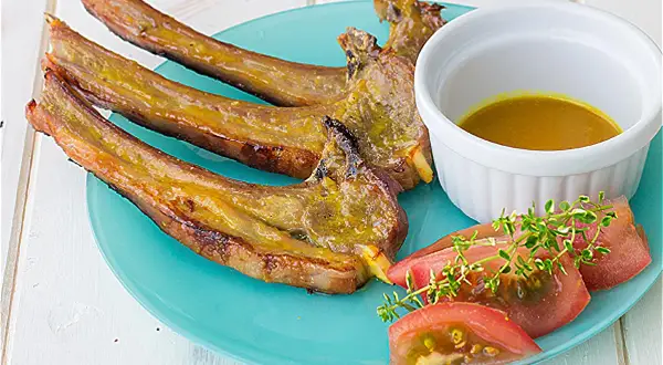 Chuletas de cordero al horno, doradas y jugosas, servidas con una salsa dorada, rodajas de tomate y ramitas de tomillo fresco.