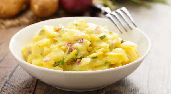 Schüssel mit cremigem Kartoffelsalat, garniert mit Schnittlauch und roten Zwiebeln. Perfekt für 7 Tassen Salat.