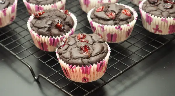 Czekoladowe muffinki z fasoli, ozdobione suszoną żurawiną, prezentują się apetycznie na czarnej kratce.