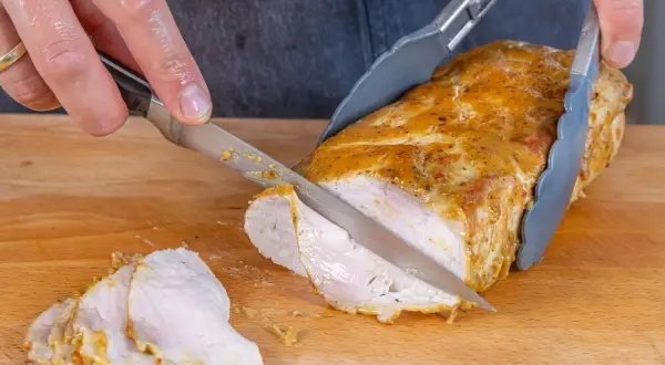 Ein saftiger Schweinelachs wird auf einem Holzbrett in Scheiben geschnitten. Die goldbraune Kruste und das zarte Fleisch sind gut sichtbar.