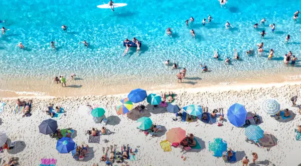 Viste aeree di spiagge di sabbia con fondale basso in Calabria, con bagnanti che si godono il sole e il mare cristallino.