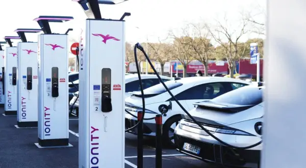Une rangée de bornes de recharge IONITY attend des véhicules électriques. Des voitures modernes sont garées, prêtes à être chargées.