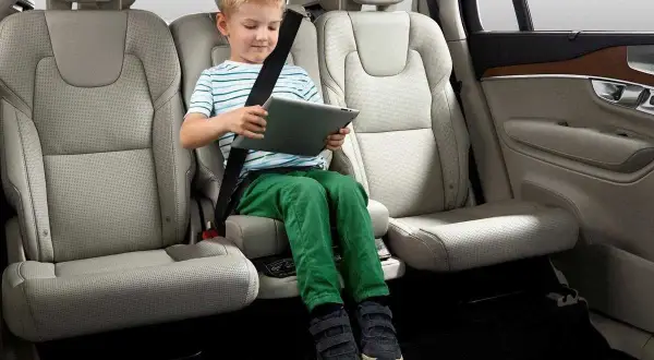 Niño en alzador coche, cumpliendo la normativa de seguridad vial. Viaja entretenido con su tablet.