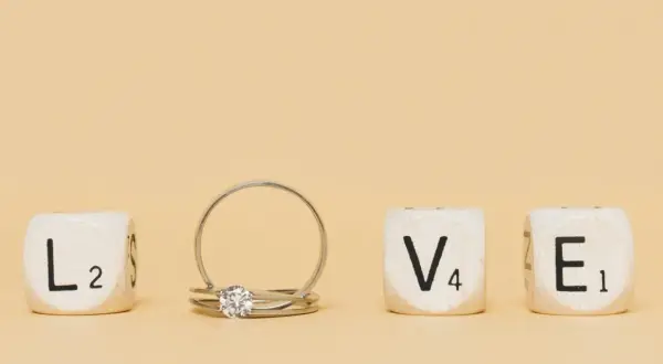 Un anillo inicial de oro con un diamante, junto a cubos que forman la palabra "LOVE".