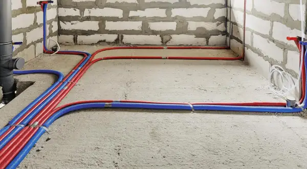 Nowa instalacja wodna w domu, z czerwonymi i niebieskimi rurami biegnącymi po betonowej podłodze i ścianach z bloczków.