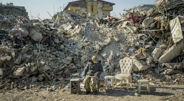 Mężczyzna siedzi wśród gruzów po trzęsieniu ziemi w Turcji. Obok niego stoją meble, jakby czekał na powrót do normalności.