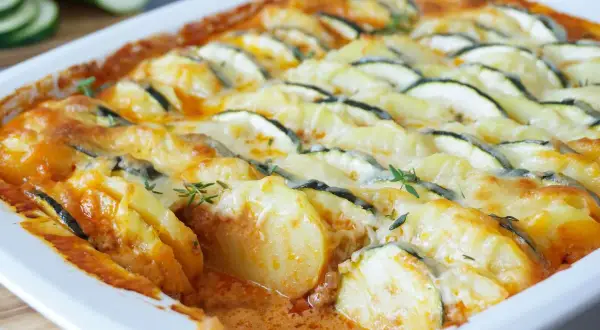 Herzhafter Zucchini Auflauf mit Kartoffeln und geschmolzenem Käse, garniert mit frischen Kräutern.