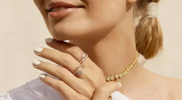 Manos con manicura blanca luciendo dos anillos de **joyería Suárez anillos** y un collar dorado.