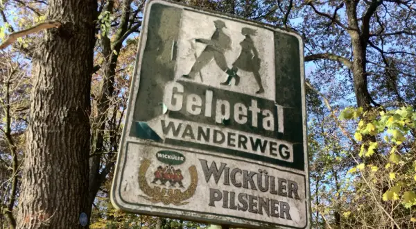 Schild am wanderparkplatz Gelpetal weist den Weg. Silhouetten von Wanderern und Bierwerbung.