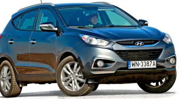 Ciemnoszary Hyundai Tucson, jeden z popularnych koreańskich samochodów, z kierowcą w czerwonej czapce za kierownicą.