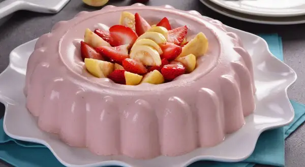 Deliciosa gelatina de fresa con trozos de fresa y guayaba fresca en el centro, servida en un plato blanco ondulado.