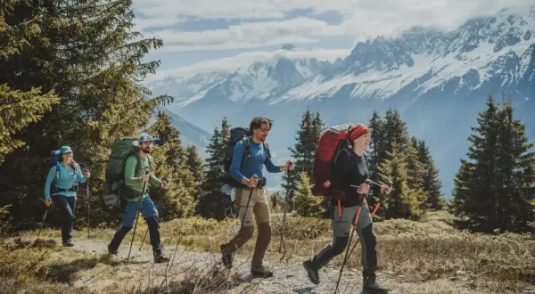 Cuatro personas con mochilas grandes caminan por un sendero montañoso. La diferencia entre senderismo y montañismo se ve en su equipo y el terreno.