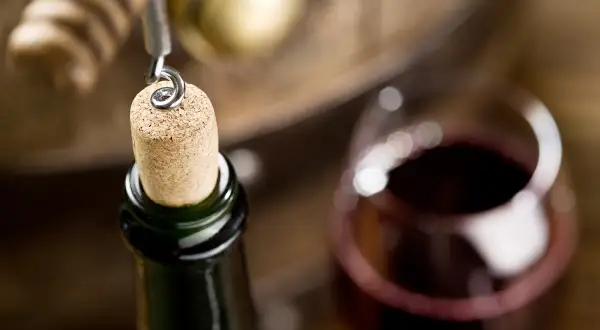 Korek wyciągany z butelki wina, obok kieliszek z czerwonym winem i beczka. Zastanawiasz się, ile może stać otwarte wino?
