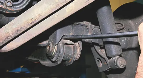 Mechanik pracuje przy wahaczu w samochodzie, używając narzędzia do regulacji.