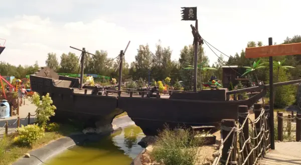 Statek piracki z czarną banderą i armatami, jak z krainy Canpol Wonderland, przecina wodny rów.