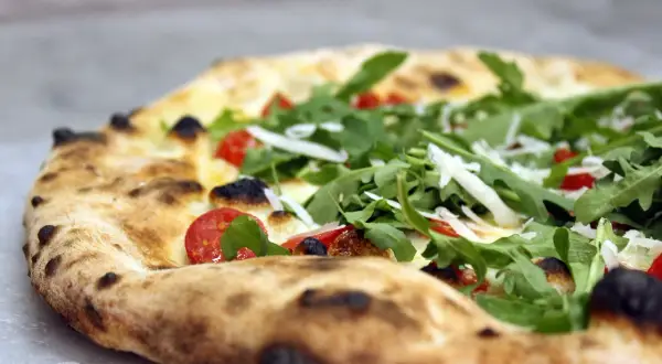 Zbliżenie na pizzę z rukolą, pomidorkami koktajlowymi i parmezanem.