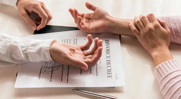 Dwie dłonie trzymają obrączki na tle dokumentu "DIVORCE DECREE". Czy do rozwodu potrzebny jest akt małżeństwa? Pytanie wisi w powietrzu.