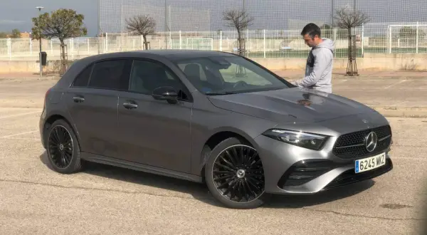 Un hombre se apoya en un elegante Mercedes Clase A gris oscuro, listo para un viaje.